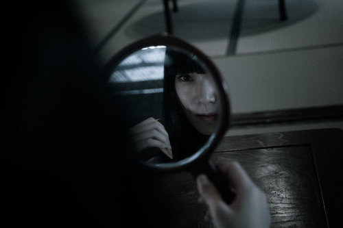 薄暗い室内で円鏡を見ながら髪をとかす女性