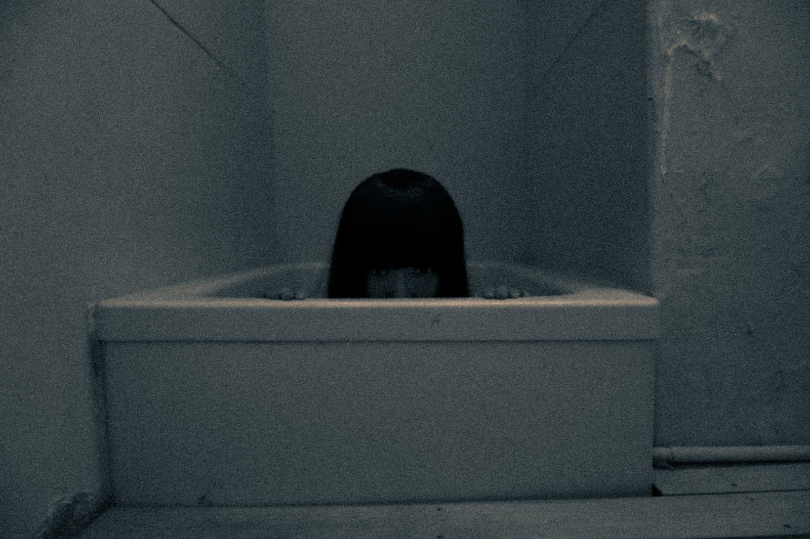 薄暗い風呂場の浴槽の底から現れる黒い髪の女性の頭部