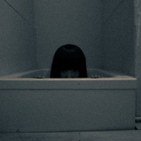 仄暗い風呂場の底から浮かぶ黒い髪の女性の頭部の写真