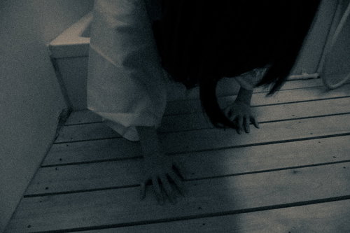 薄暗い空間のすのこの上を這う白い衣装の女性