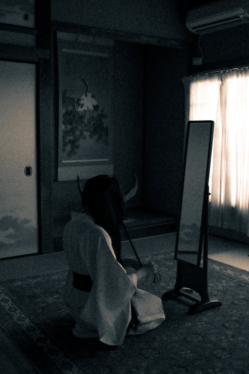 薄暗い部屋で姿見鏡の前に正座し、髪を解いている女性の後ろ姿