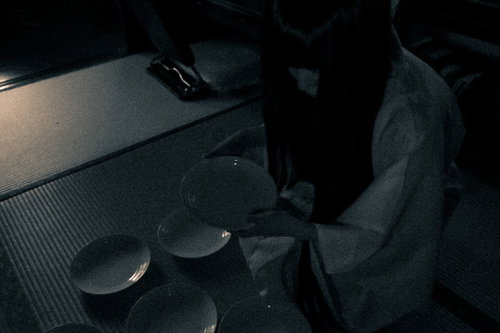 暗い空間で白い皿を物色する不気味な女性の表情