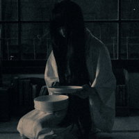 薄暗い室内で正座して皿を見つめる不気味な女性の写真