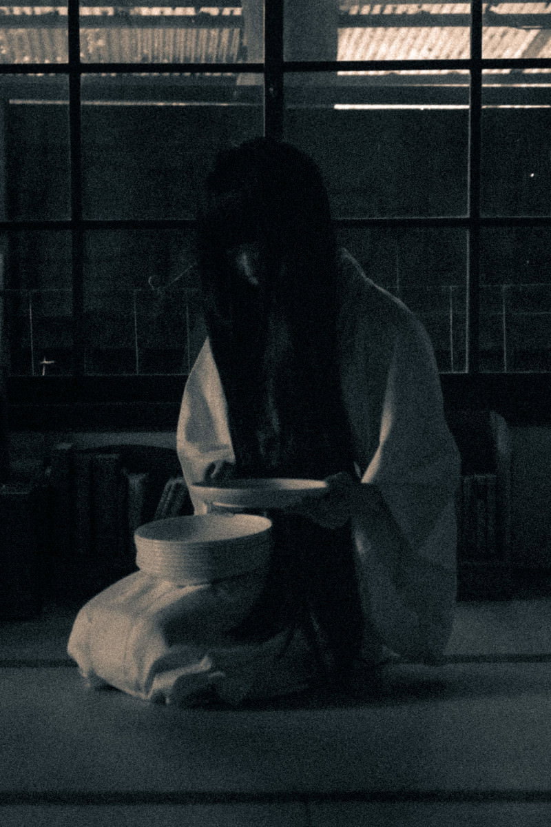 薄暗い室内で正座をして皿を見つめる不気味な女性［モデル：緋真煉］
