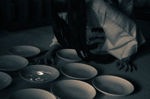 薄暗い空間で皿を見つめる不気味な女性の恐怖表現
