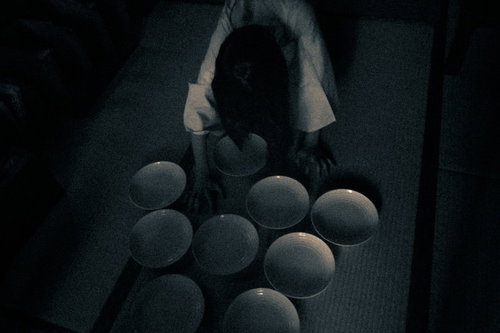 暗がりの中でお皿を並べる不気味なゆうれいのシルエット