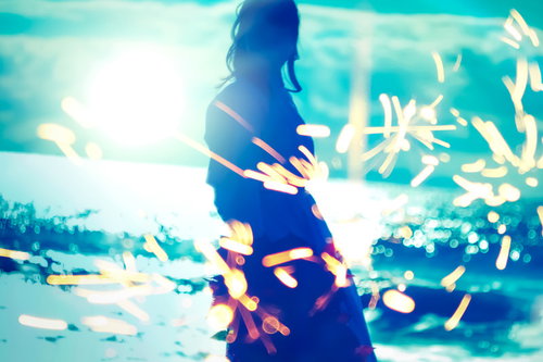 夕暮れの海岸で弾ける火花と佇む女性のシルエット