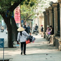 ハノイ市街で荷物を背負って立つ売り子の街頭販売風景の写真