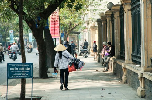 ハノイ市街で荷物を背負って立つ売り子の街頭販売風景