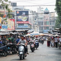 ホーチミンの活気あるマーケット街を走行するバイクと人混みの写真