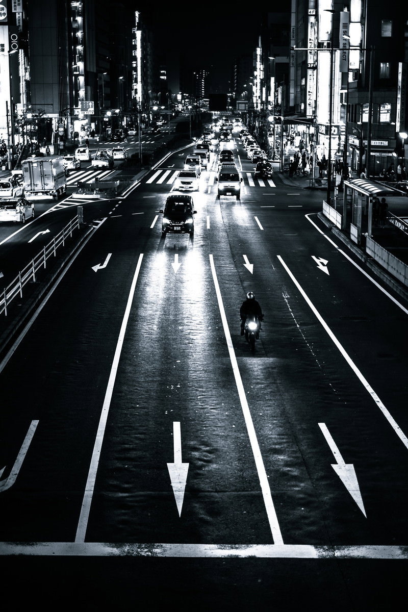 夜の交差点で走行する自動車と二輪車、照らされた街並み