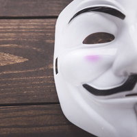 木製テーブルに置かれた無表情の白い仮面、サイバーセキュリティ関連の写真