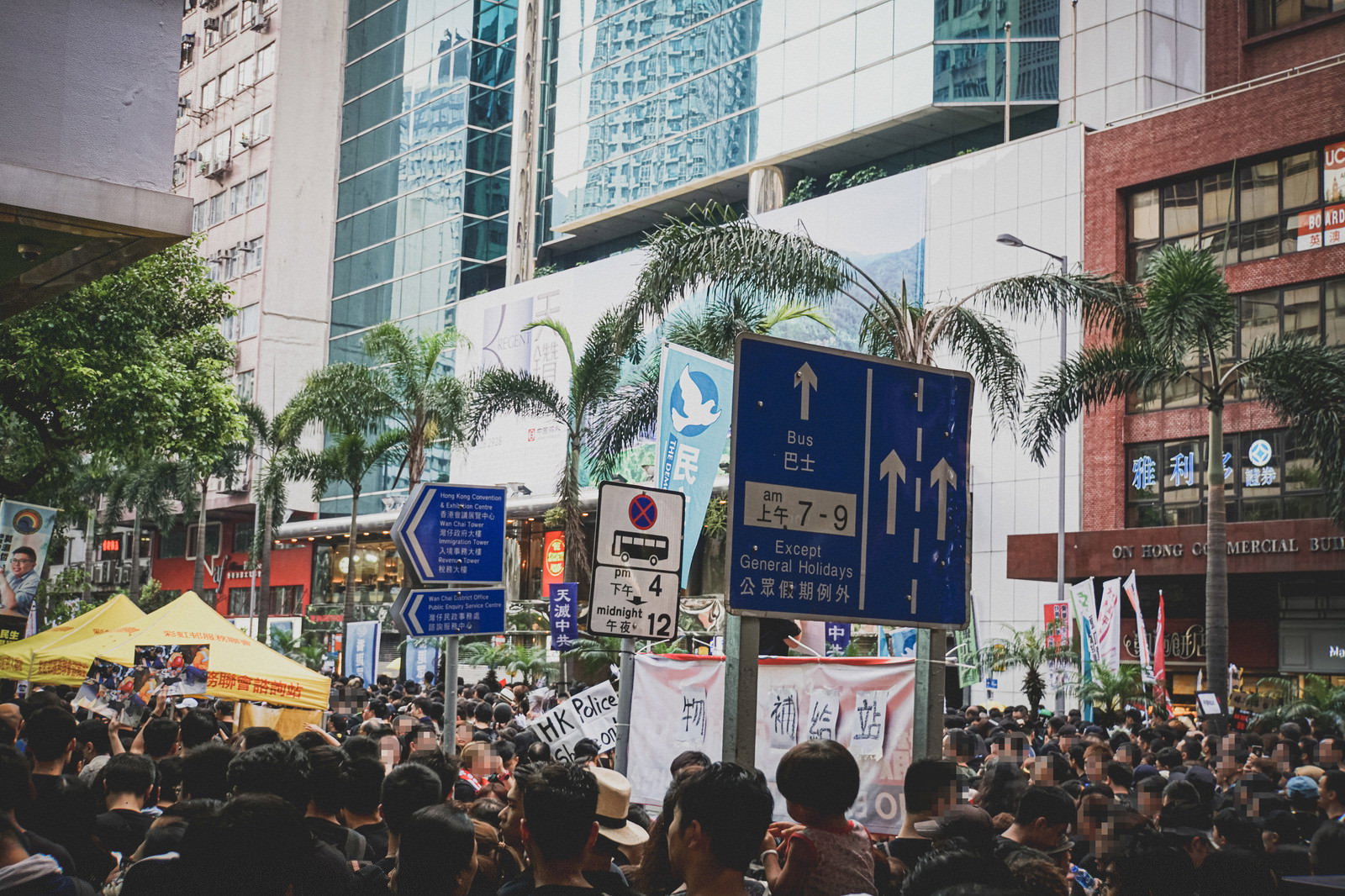 香港の街頭で黒い服装の大人数が密集し、プラカードを掲げながら行動している群衆の光景