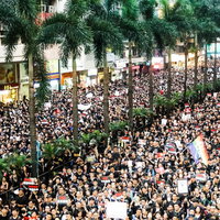 香港の屋外集会に集う数千人の参加者と白い横断幕の群衆の写真