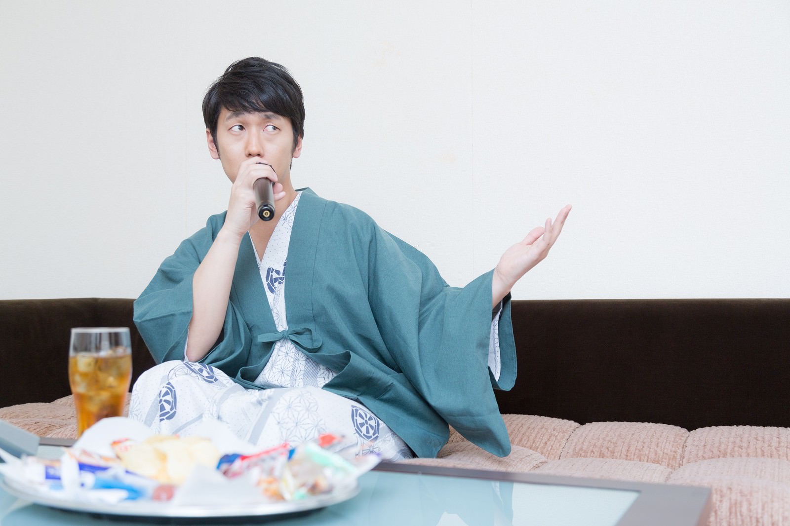 青い浴衣を着た男性がソファーでマイクを持ってカラオケをしている［モデル：大川竜弥］