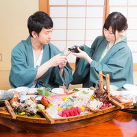 伊東温泉旅館で豪華な舟盛りを前にお酌する二人の写真
