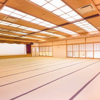 畳敷きにステージと障子窓がある温泉旅館の木製天井の大宴会場の写真