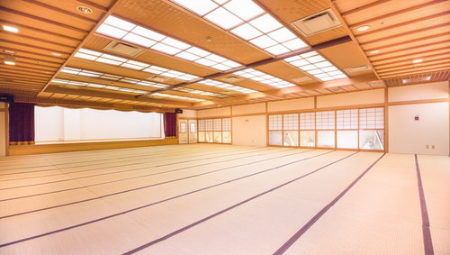 畳敷きにステージと障子窓がある温泉旅館の木製天井の大宴会場