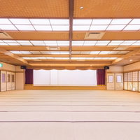 白い壁のステージと紫のカーテンがある畳敷きの大宴会場の写真