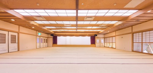 白い壁のステージと紫のカーテンがある畳敷きの大宴会場