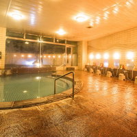 緑色の湯が張られた大浴槽と白い椅子の洗い場がある旅館の大浴場の写真