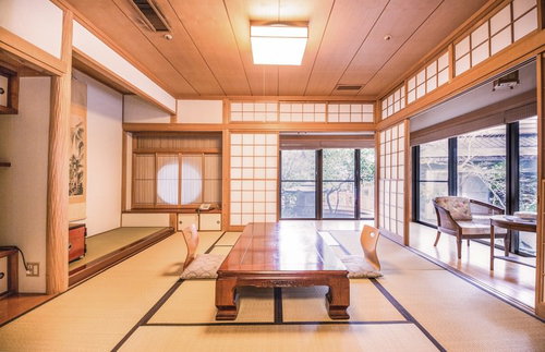 障子の引き戸と木枠の窓から自然光が入る畳に低いテーブルの温泉宿の和室
