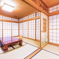 格子状の木枠障子と照明器具がある畳にテーブルと座布団の和室の写真