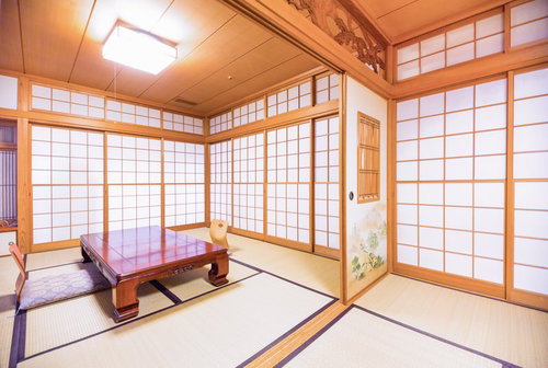 格子状の木枠障子と照明器具がある畳にテーブルと座布団の和室