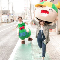 女性レポーターに頭部を奪われたゆるキャラと後ろで驚く男性の写真