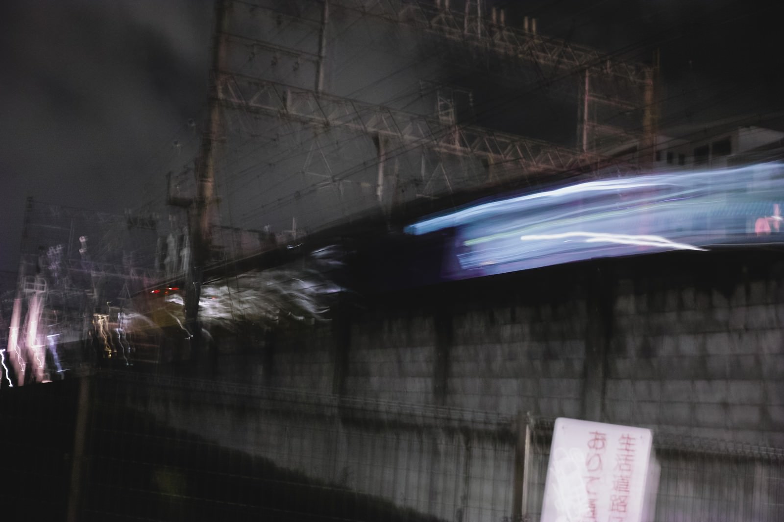 夜間に線路を走行する青白く光る電車が通過する駅舎の写真