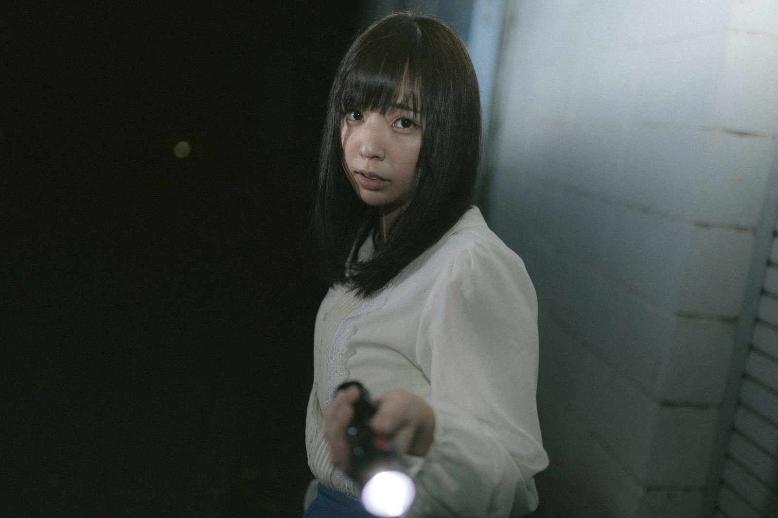 暗闇の中でハンドライトを持って探索する白い服の女性