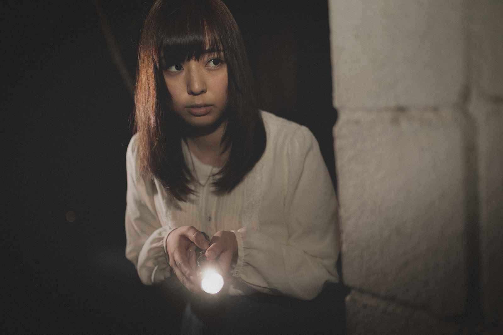 懐中電灯を持って暗い廃墟を探索する女性［モデル：さとうゆい］