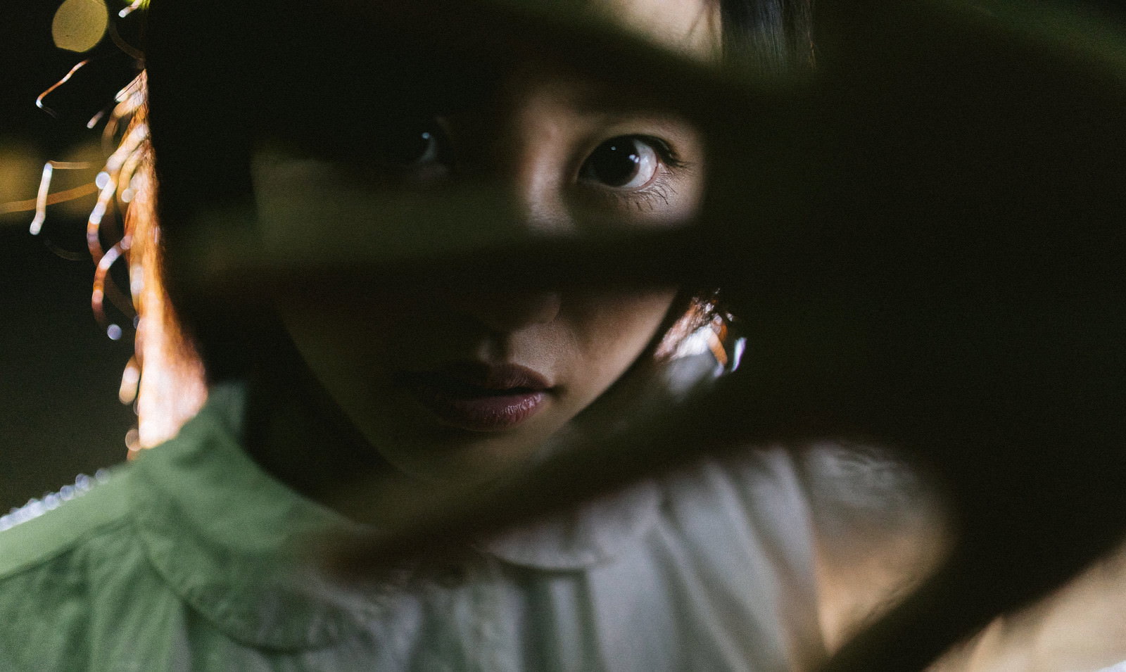 暗い室内で両手で顔を隠す女性［モデル：河村友歌］