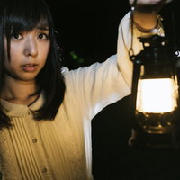 ランタンを片手に暗闇を歩く不安そうな表情の女性の写真