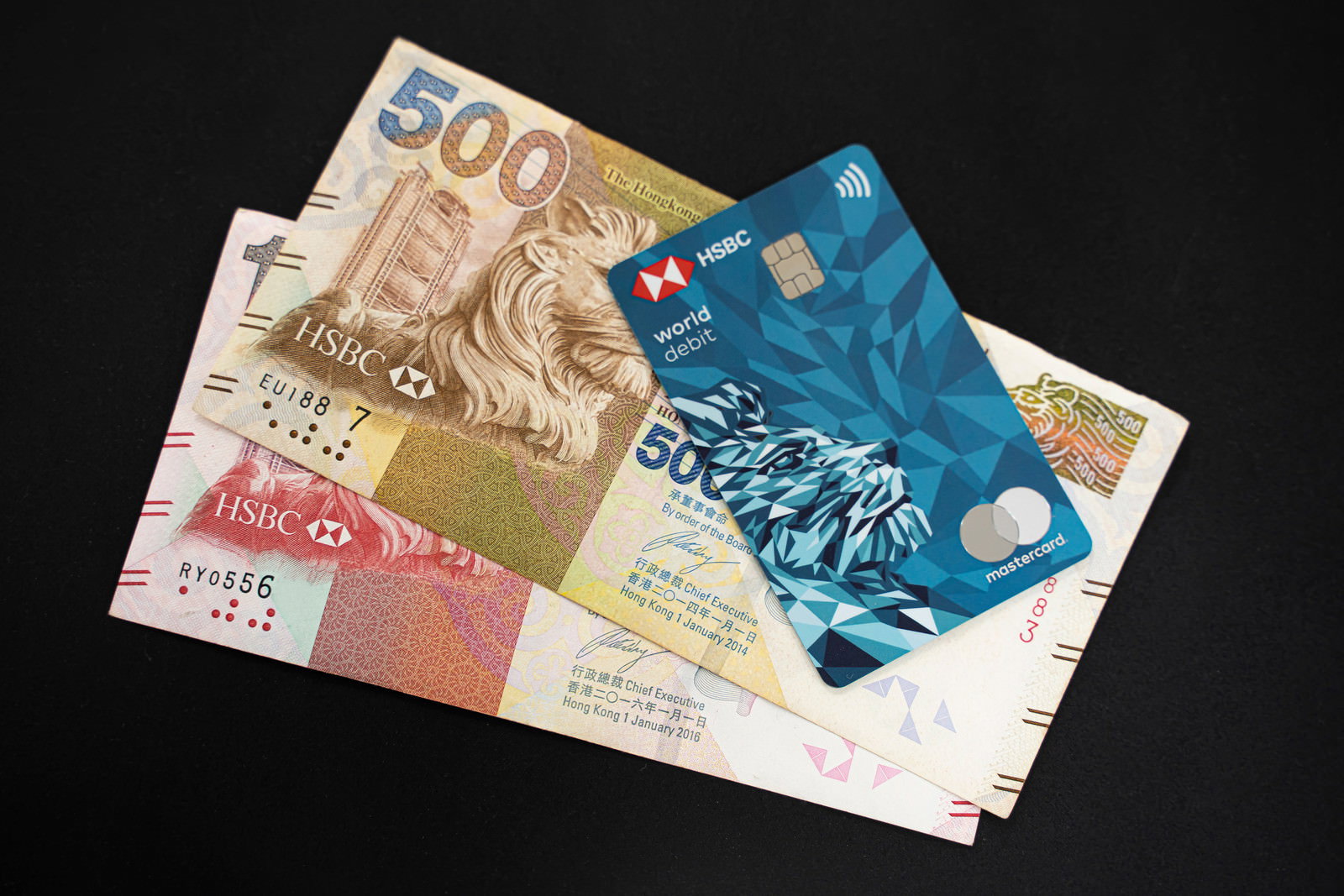 黒い背景に香港ドル紙幣とHSBCデビットカードが重なって置かれている