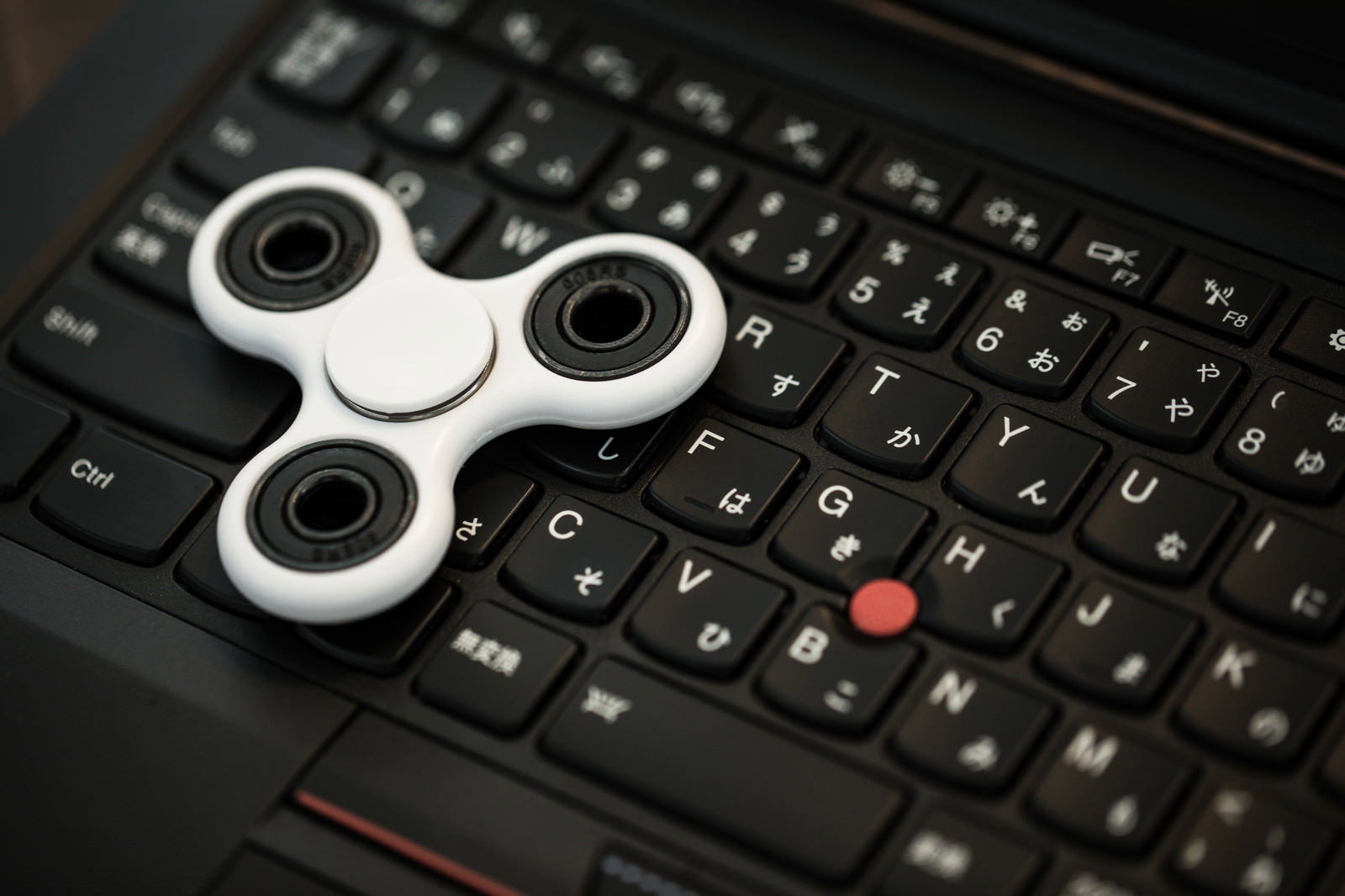 黒いノートパソコンのキーボード上に置かれた白いハンドスピナー