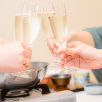 明るい室内のテーブルで3人がワイングラスを合わせる旅館の鍋料理の乾杯の写真