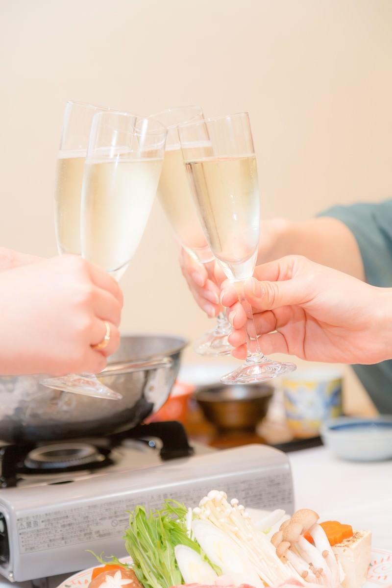明るい室内のテーブルで3人がワイングラスを合わせる旅館の鍋料理の乾杯