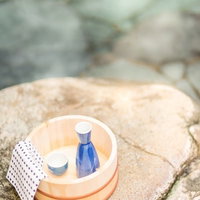 石畳の上に木の桶に入った青い瓶と小さな器と水玉模様の布の写真