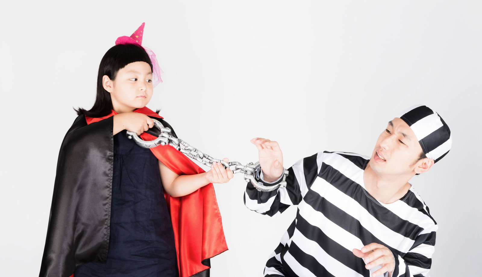囚人服の父と魔法使いコスプレの娘がチェーンで遊ぶハロウィンの写真［モデル：大川竜弥 ゆうき］