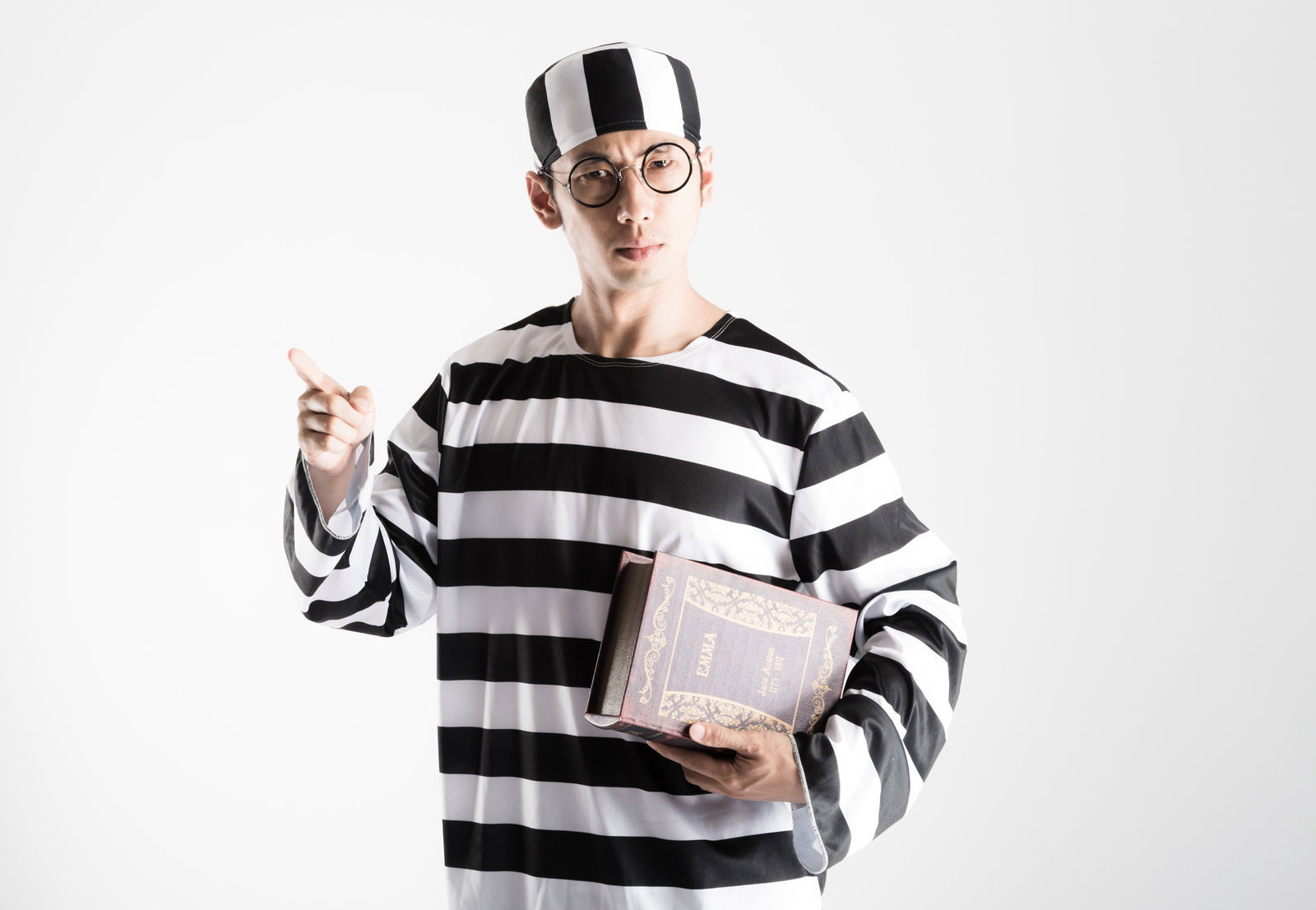黒白ボーダー柄シャツの囚人コスプレ男性が本を持ち指を突き出している［モデル：大川竜弥］
