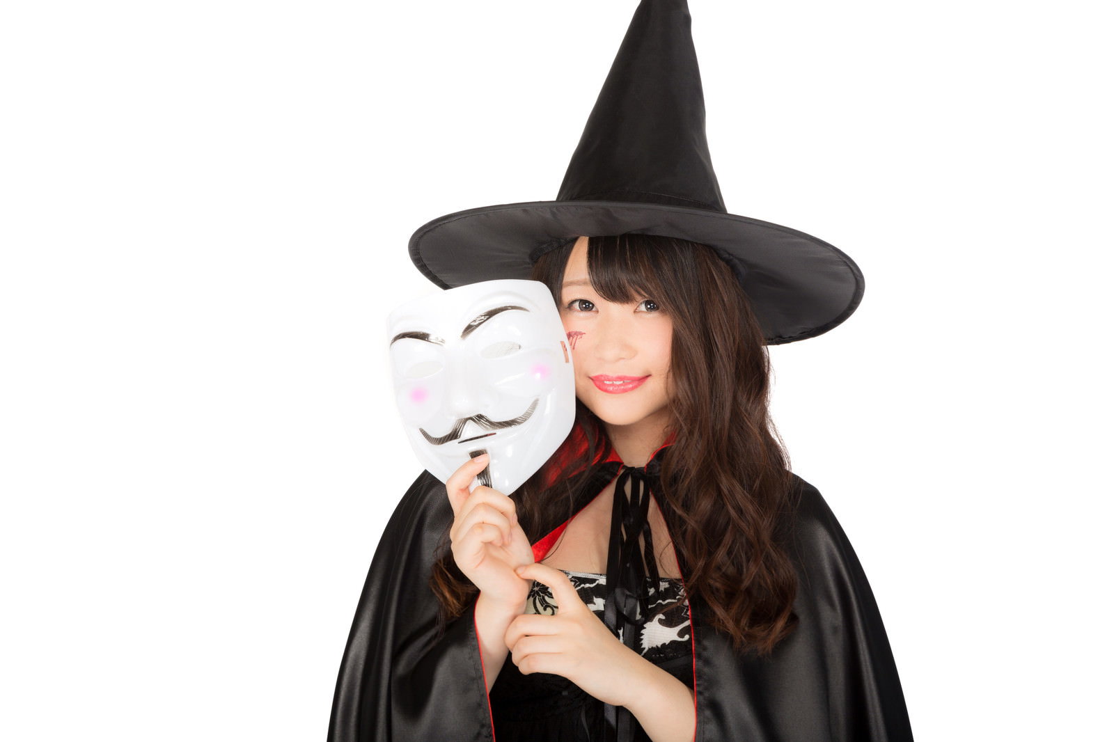 黒いとんがり帽子とマントの魔女姿で白いマスクを持つ女性［モデル：茜さや］