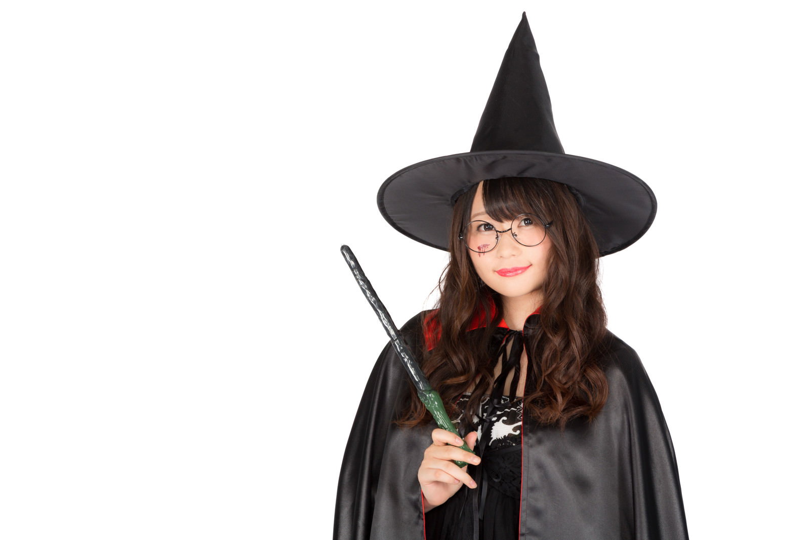 黒いとんがり帽子とステッキを持つ魔女コスプレの女性が、右手を上げて魔法をかけるポーズをしている［モデル：茜さや］