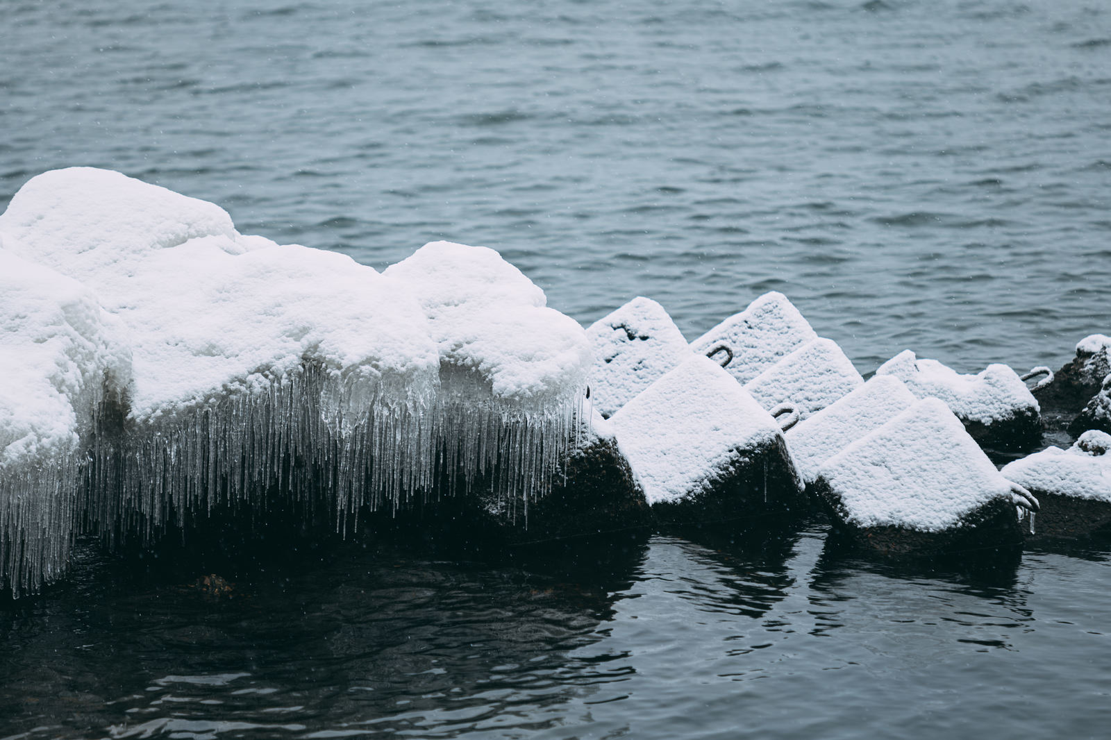 猪苗代湖の岩に積もった雪と小さなつらら、しぶき氷が見える冬の湖畔