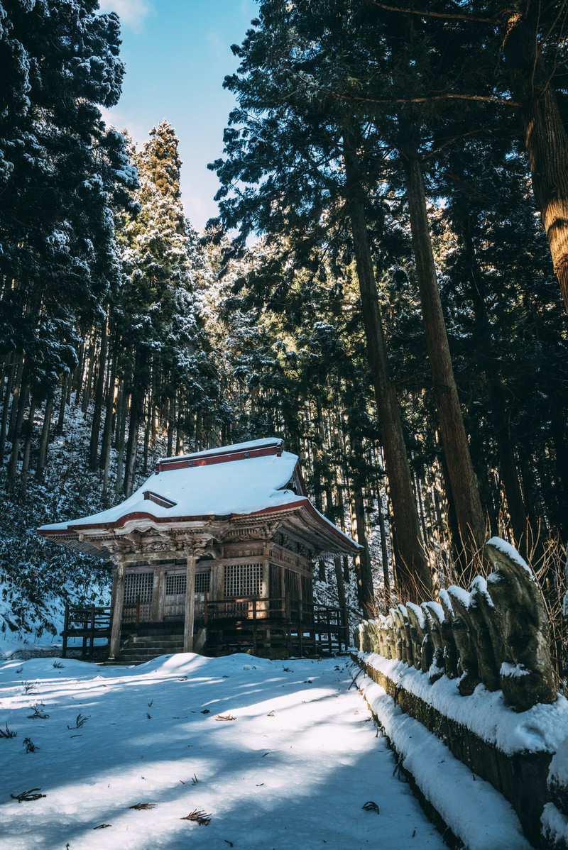 雪に覆われた観音堂と杉林