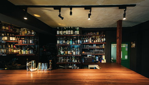 シーリングライトに照らされた木製バーのカウンターと酒棚
