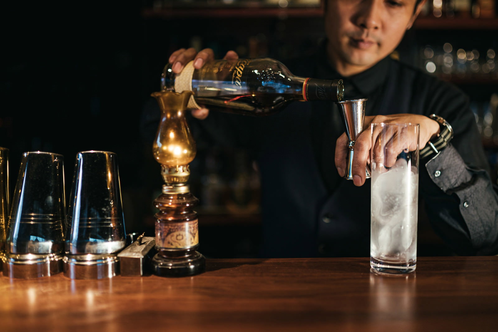 暖かい照明の下でメジャーカップを使ってお酒を計量するバーテンダー