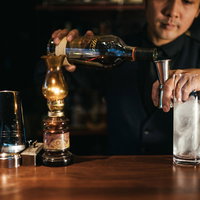 暖色照明の中でメジャーカップを使ってお酒を計量するバーテンダーの写真