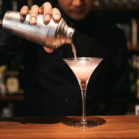 コスモポリタンカクテルをシェーカーからグラスに注ぐバーテンダーの手元の写真