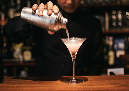 コスモポリタンカクテルをシェーカーからグラスに注ぐバーテンダーの手元